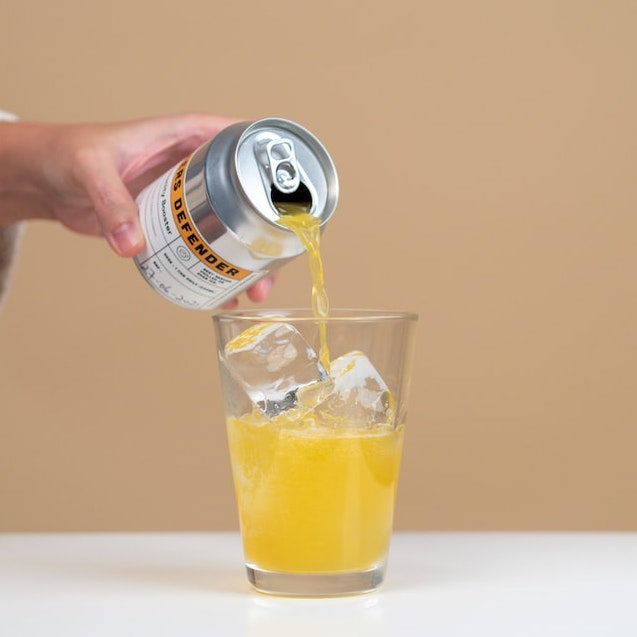 A hand pouring a canned drink into a glass of ice