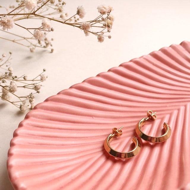 A pair of earrings on a pink plate, beside small white flowers