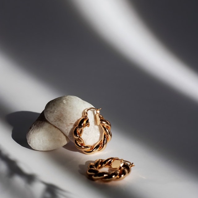 A pair of earrings resting on a stone with shadows casted on them
