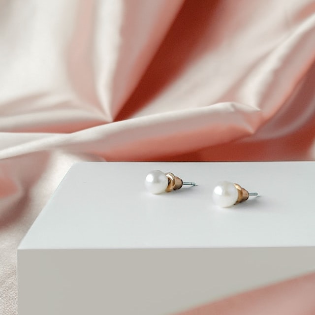 A pair of earrings on a white box, with pink silky cloth in the background